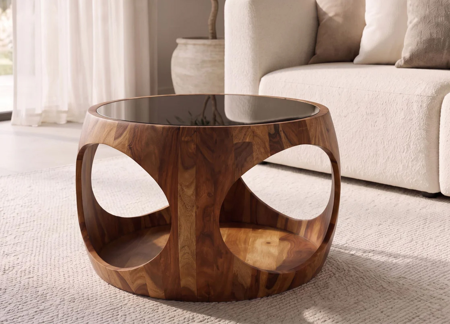 Vue de face de la table basse ronde KARSA en sheesham avec ouvertures organiques et plateau en verre noir